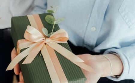 Cadeau élégant vert, ruban doré et eucalyptus tenu dans les mains | Elegant green gift, gold ribbon and eucalyptus held in hands 